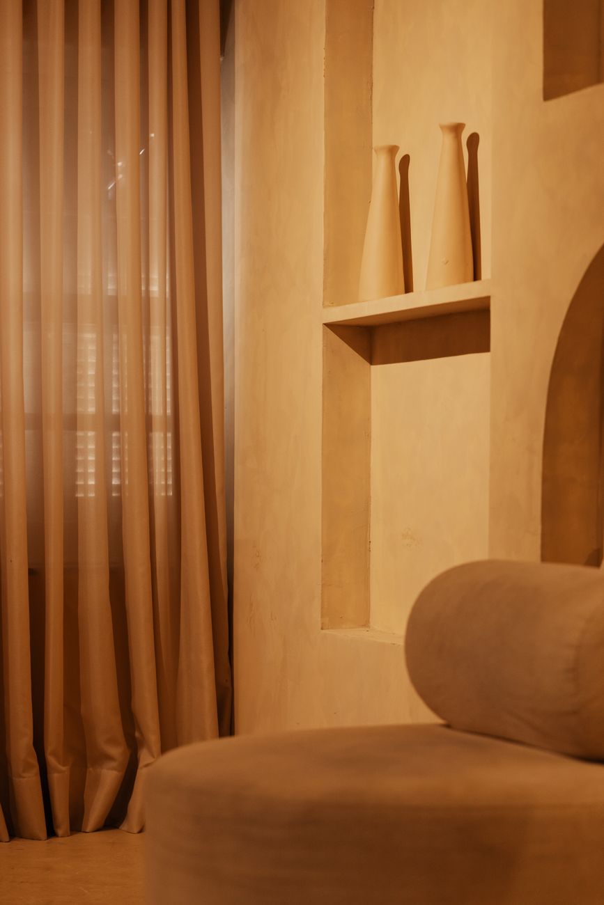 A warm plaster room with a curtained window and a low niche